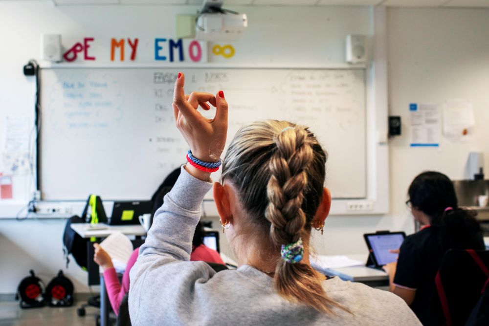Jente som sitter i klasserom og rekker opp hånden